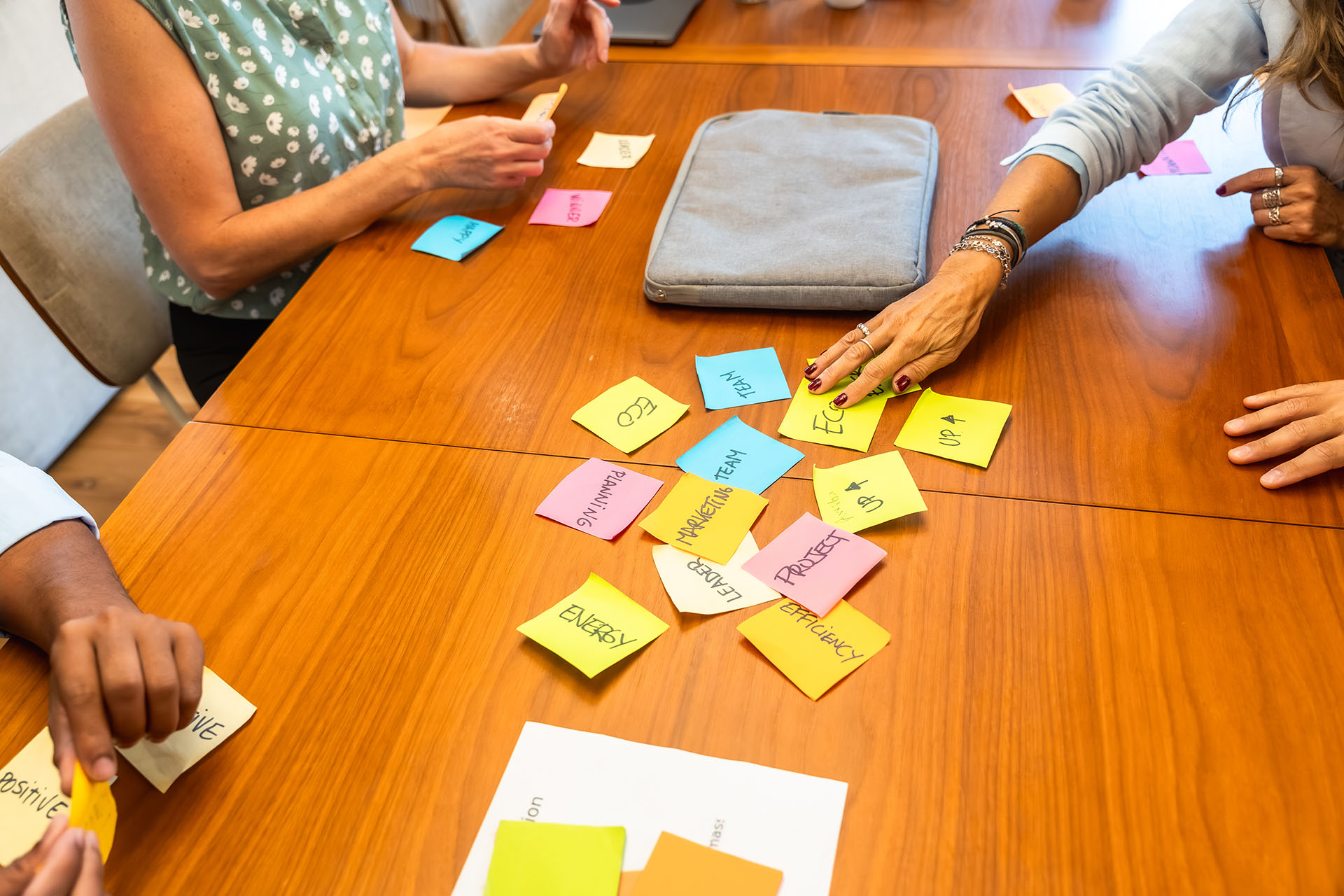 Group of people collaborating at a wooden workdesk by arranging sticky notes.