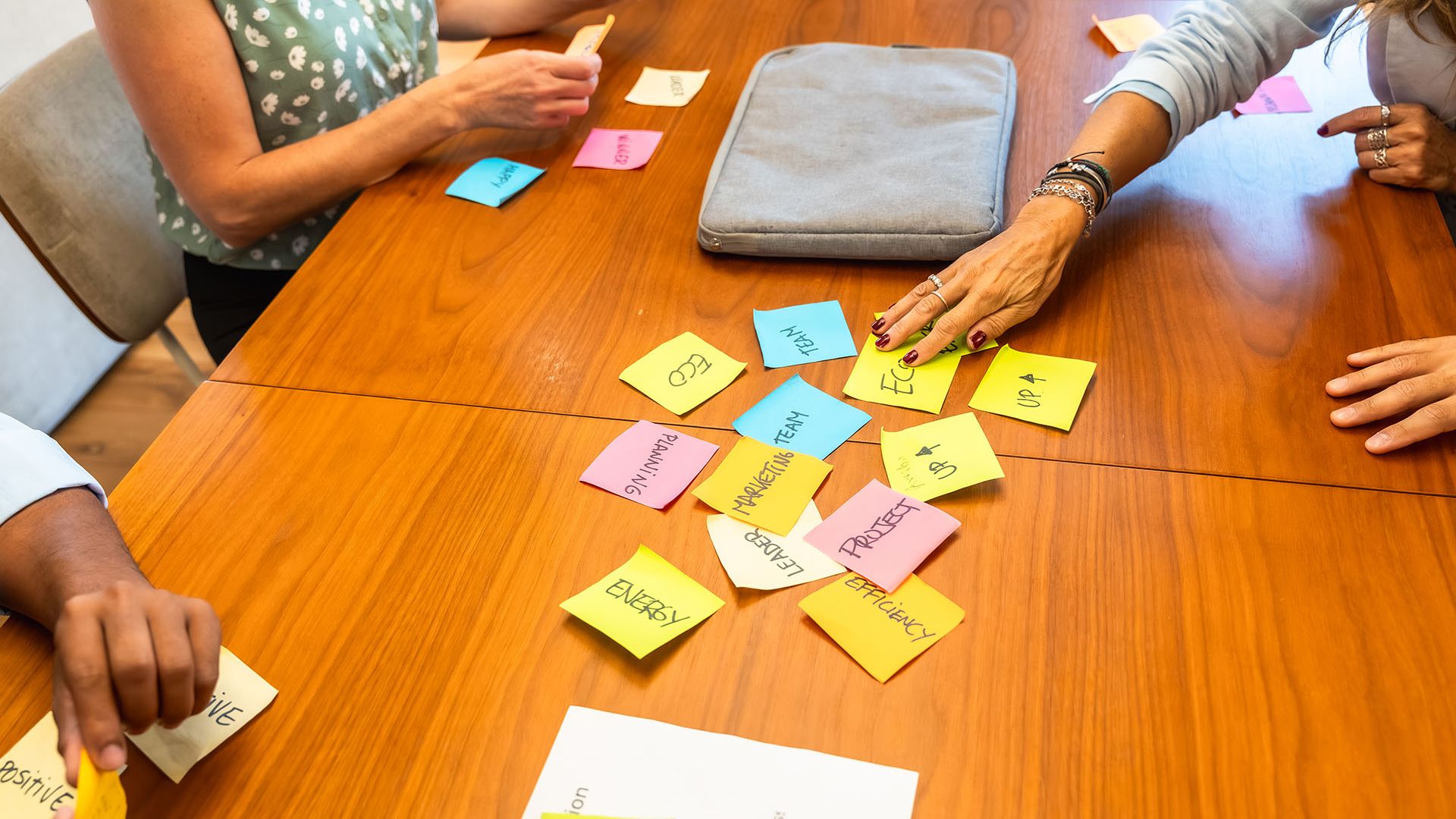 Group of people collaborating at a wooden workdesk by arranging sticky notes.