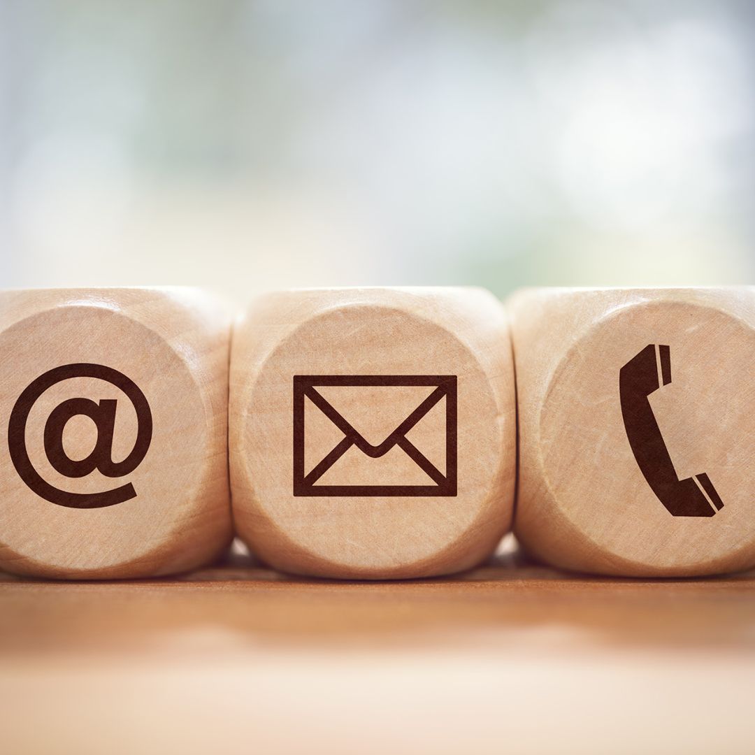 Picture of three wooden blocks with symbols: the first block shows ‘@’ for email, the second shows a mail icon for digital or paper mail, and the third shows a traditional phone receiver for phone calls.